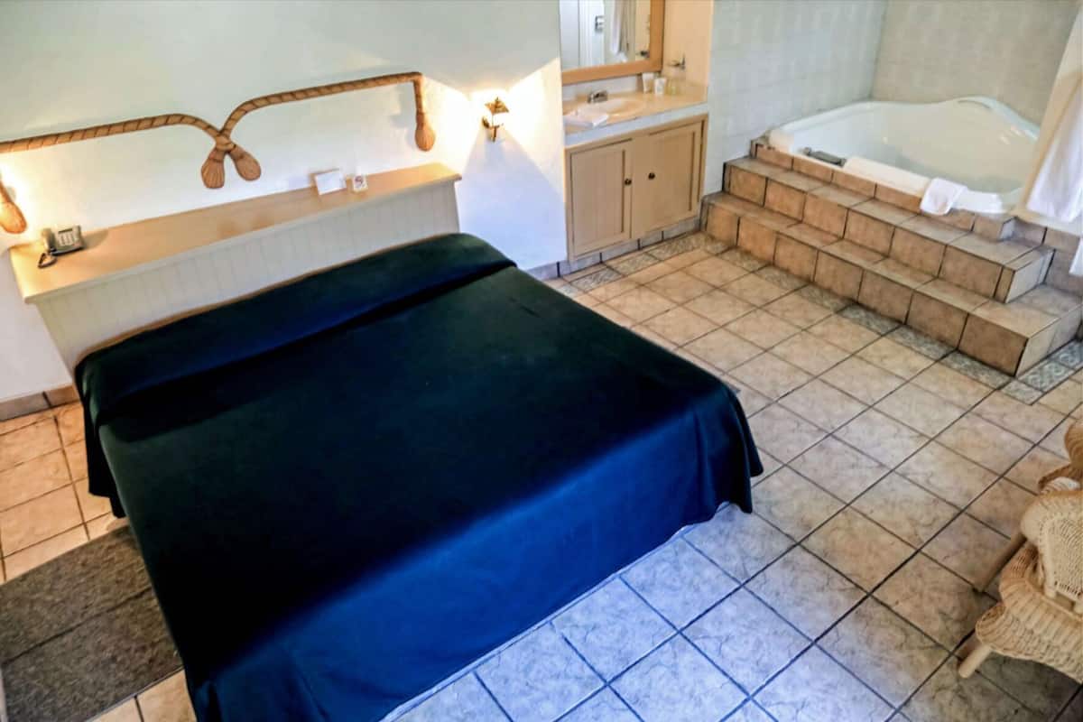 A bedroom with a bed, a bathroom with a bathtub, and a staircase leading to a shower area.