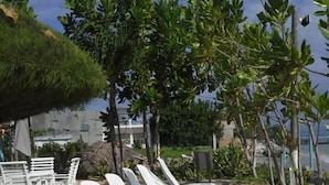 A row of white lounge chairs lined up on a concrete surface, with a thatched roof structure and greenery in the background. - Ocho Rios Villa at Coolshade VI (St. Ann's Bay)