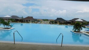 A large swimming pool with two metal ladders, surrounded by palm trees and houses with sloped roofs. - Ocho Rios Villa at Coolshade VI (St. Ann's Bay)