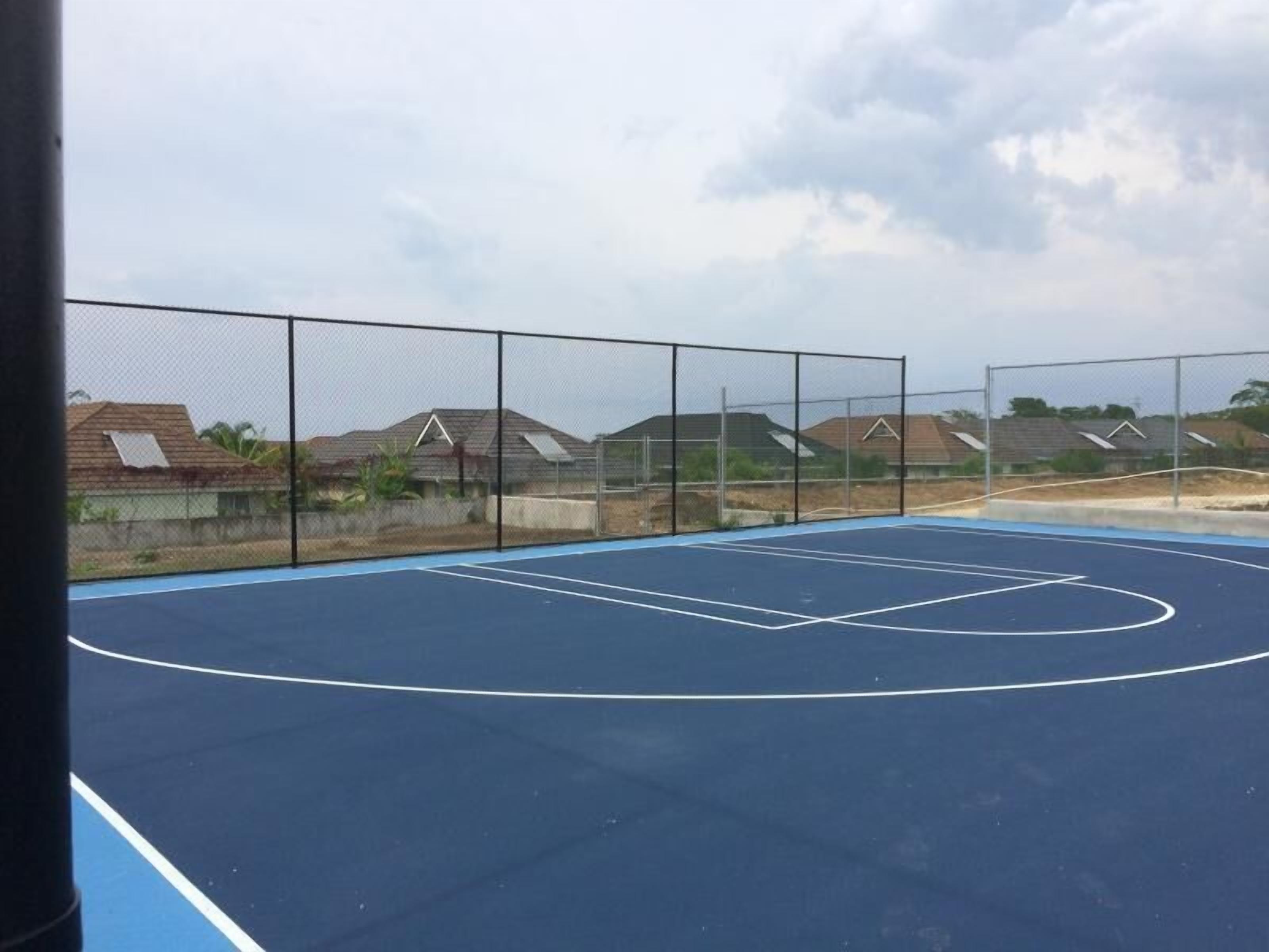 Een basketbalveld buiten, met een blauwe ondergrond en witte lijnen, omheind door een hek van gaas.