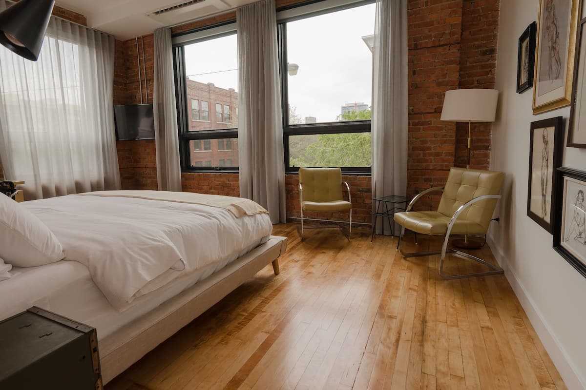 A hotel room with a bed, a chair, a table, and a window with curtains.