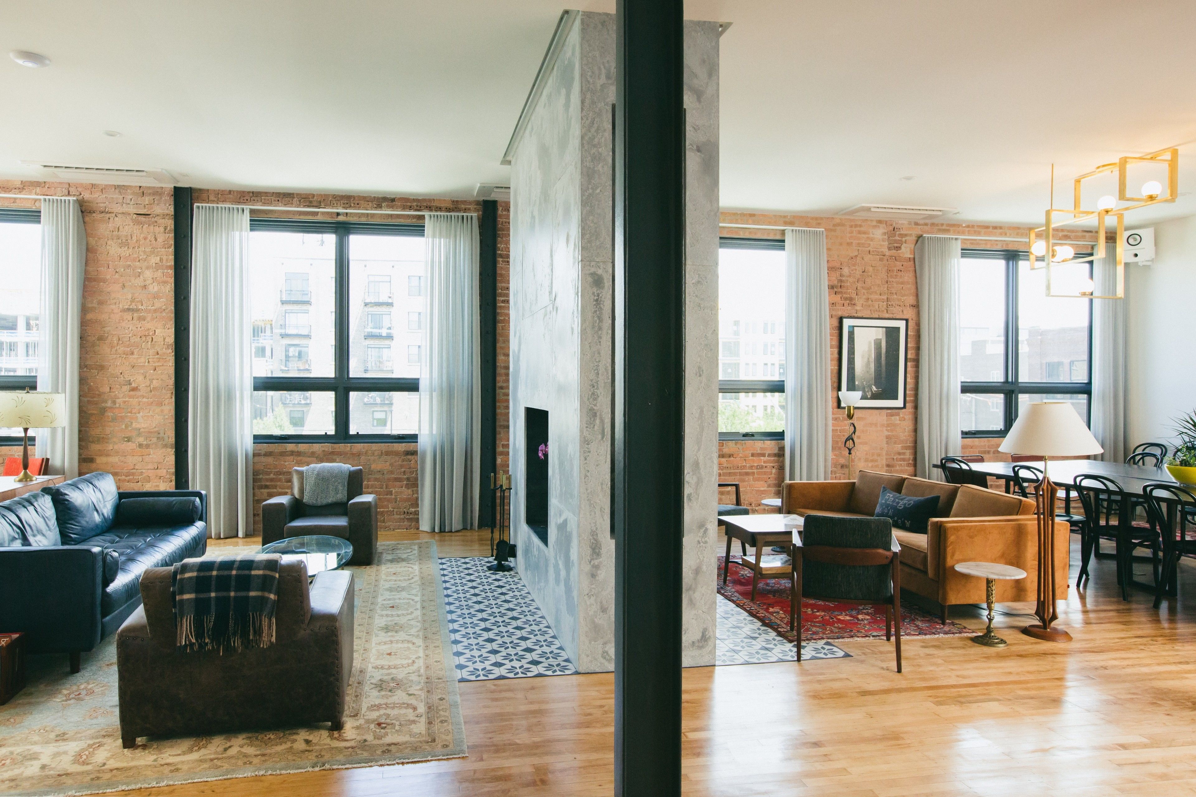 A modern living room with a fireplace, leather sofas, a dining area, and large windows with curtains.