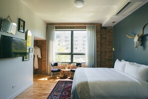 Una habitación de hotel moderna con una cama grande, una pared de ladrillo, un ventanal con cortinas y un televisor montado en la pared, además de un cráneo de toro decorativo.
