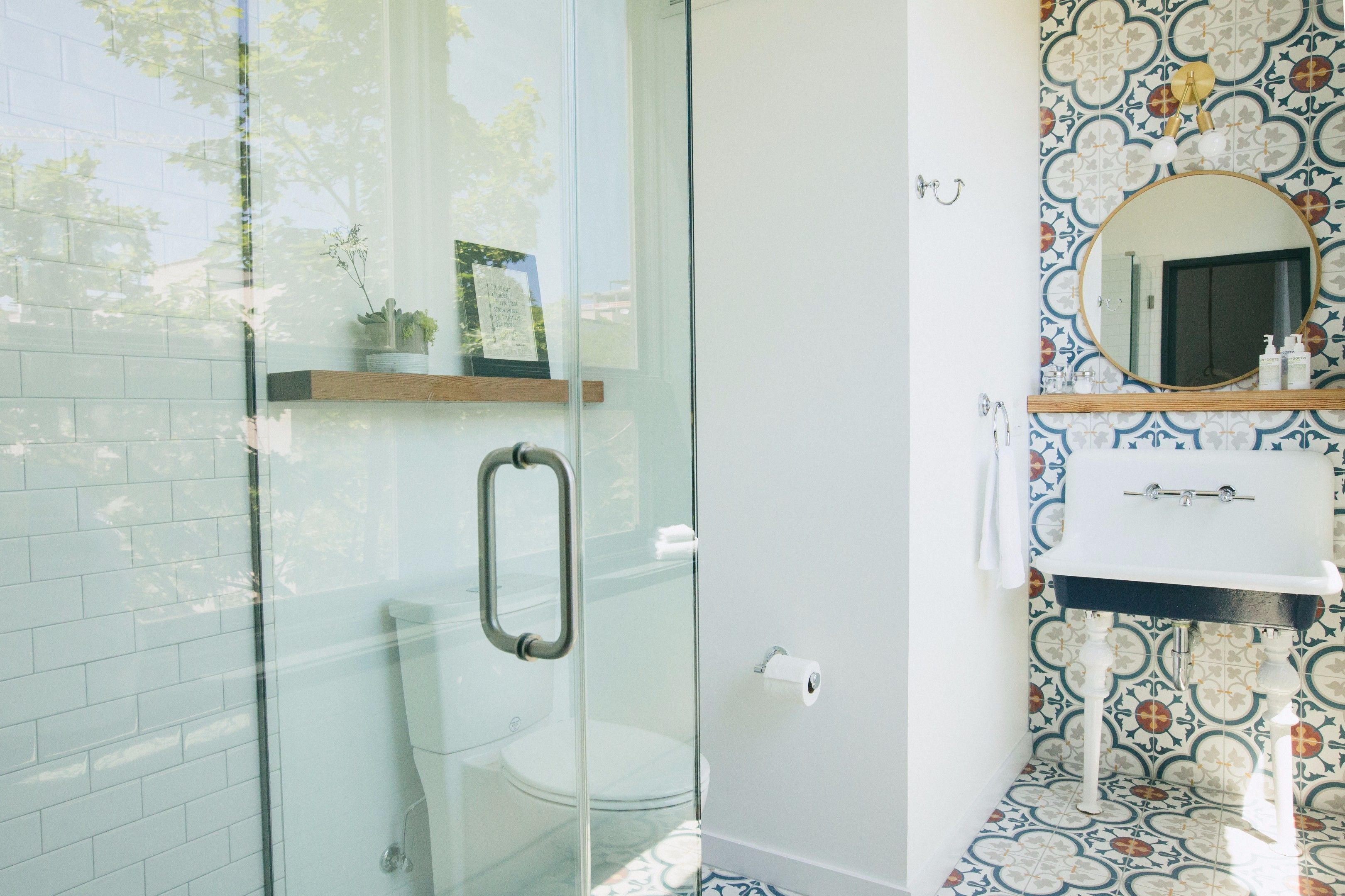 A bathroom with a glass shower enclosure, a white toilet, a sink with a mirror, and a patterned backsplash.