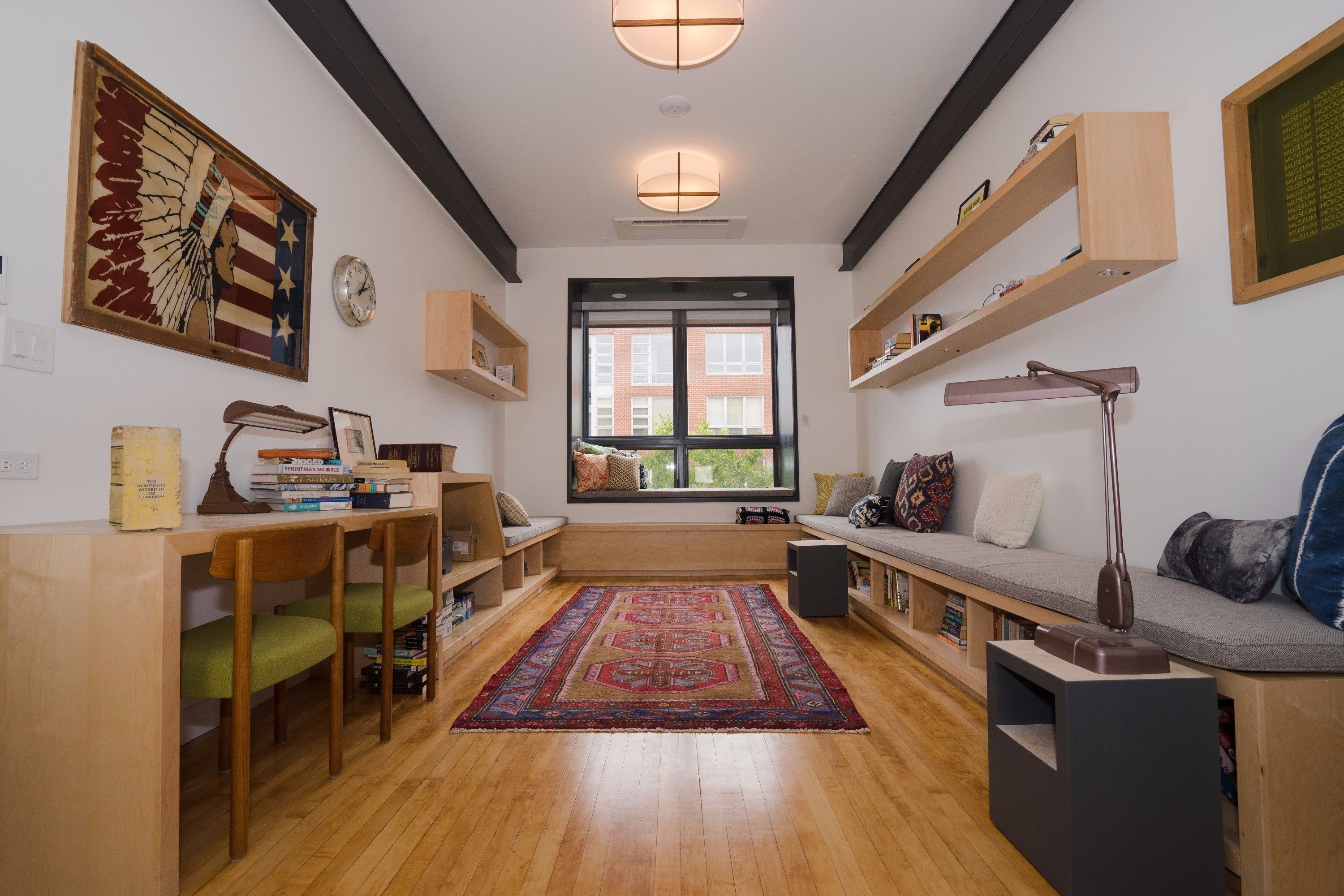 A modern living room with a wooden floor, a large window, a sofa, a desk, and shelves.
