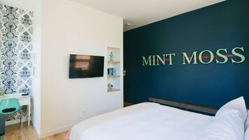 A bedroom with a bed, a desk, a chair, a TV, and a wall with the text "MINT MOSS".