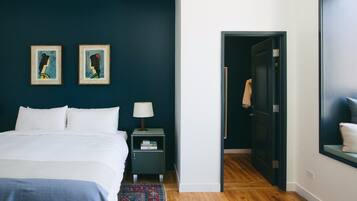 Une chambre à coucher avec un lit, deux œuvres d’art encadrées, une table de chevet, une lampe et un tapis à motifs.