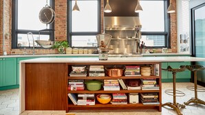 A kitchen with a large island, hanging kitchen tools, and a brick wall. - The Publishing House B&B (Chicago)
