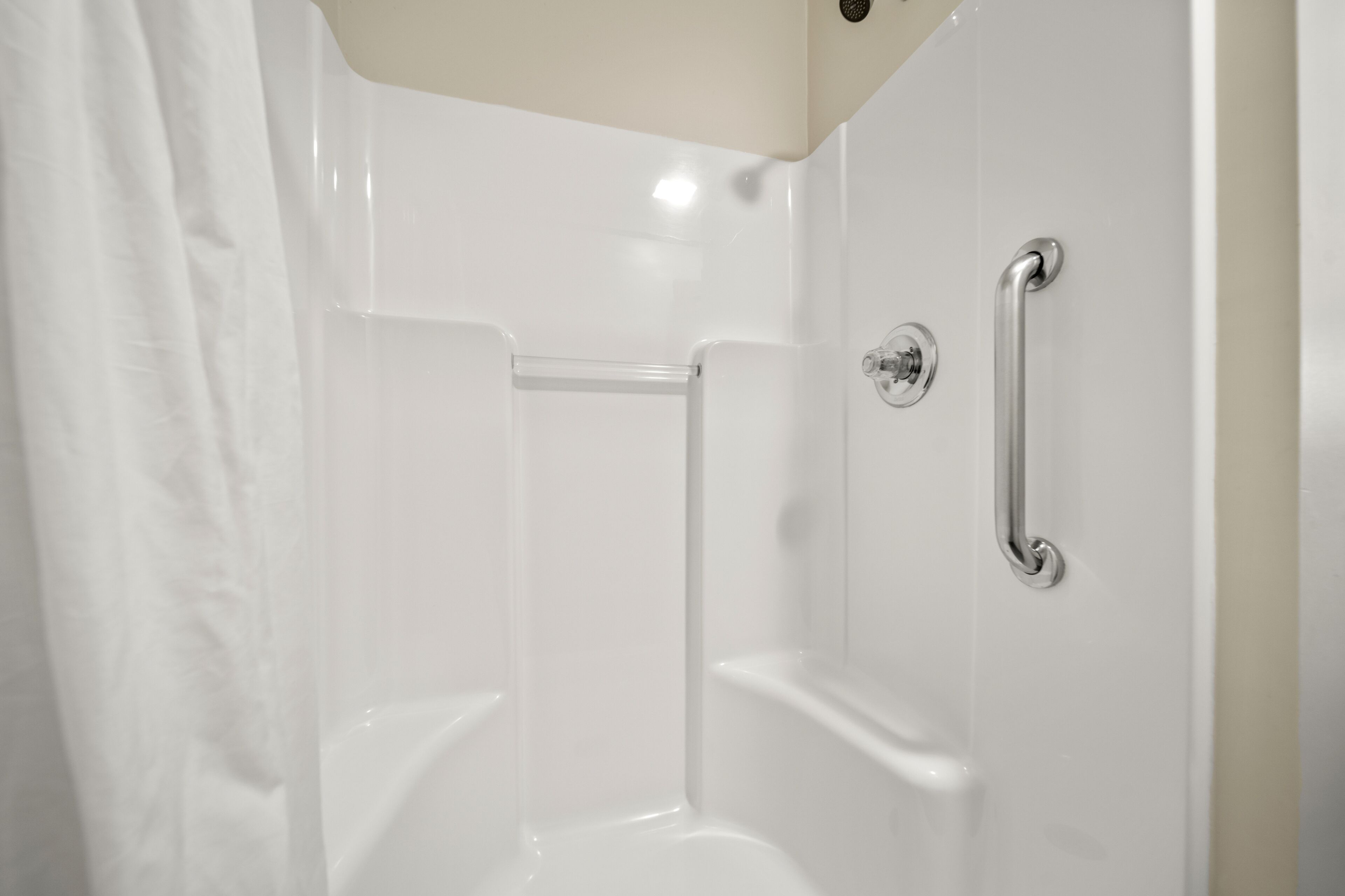 A white, empty shower stall with a grab bar and a shower curtain.