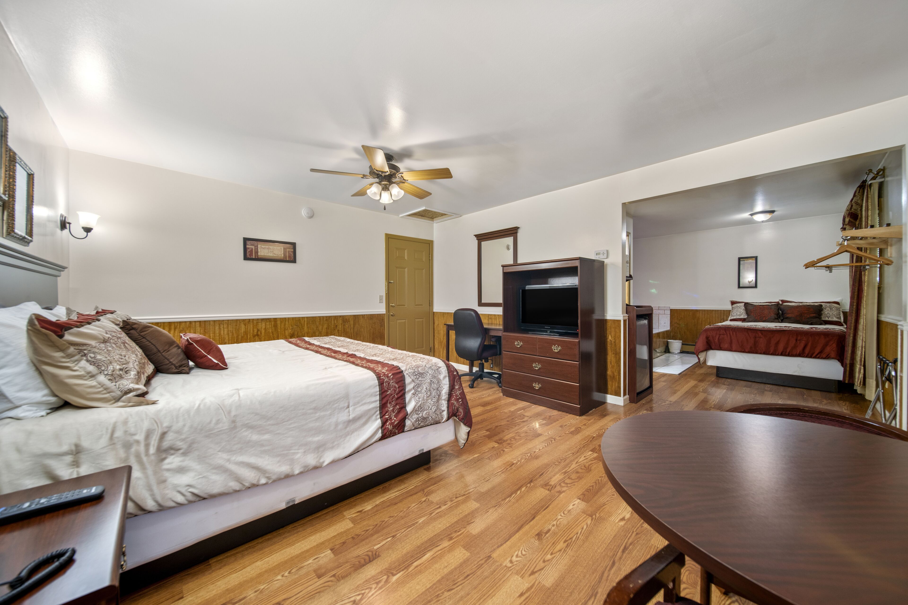 A bedroom with a bed, a desk, a TV, and a ceiling fan.
