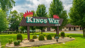 En skylt för Kings Way Inn med en kronlogotyp, omgiven av välskött trädgård och träd.