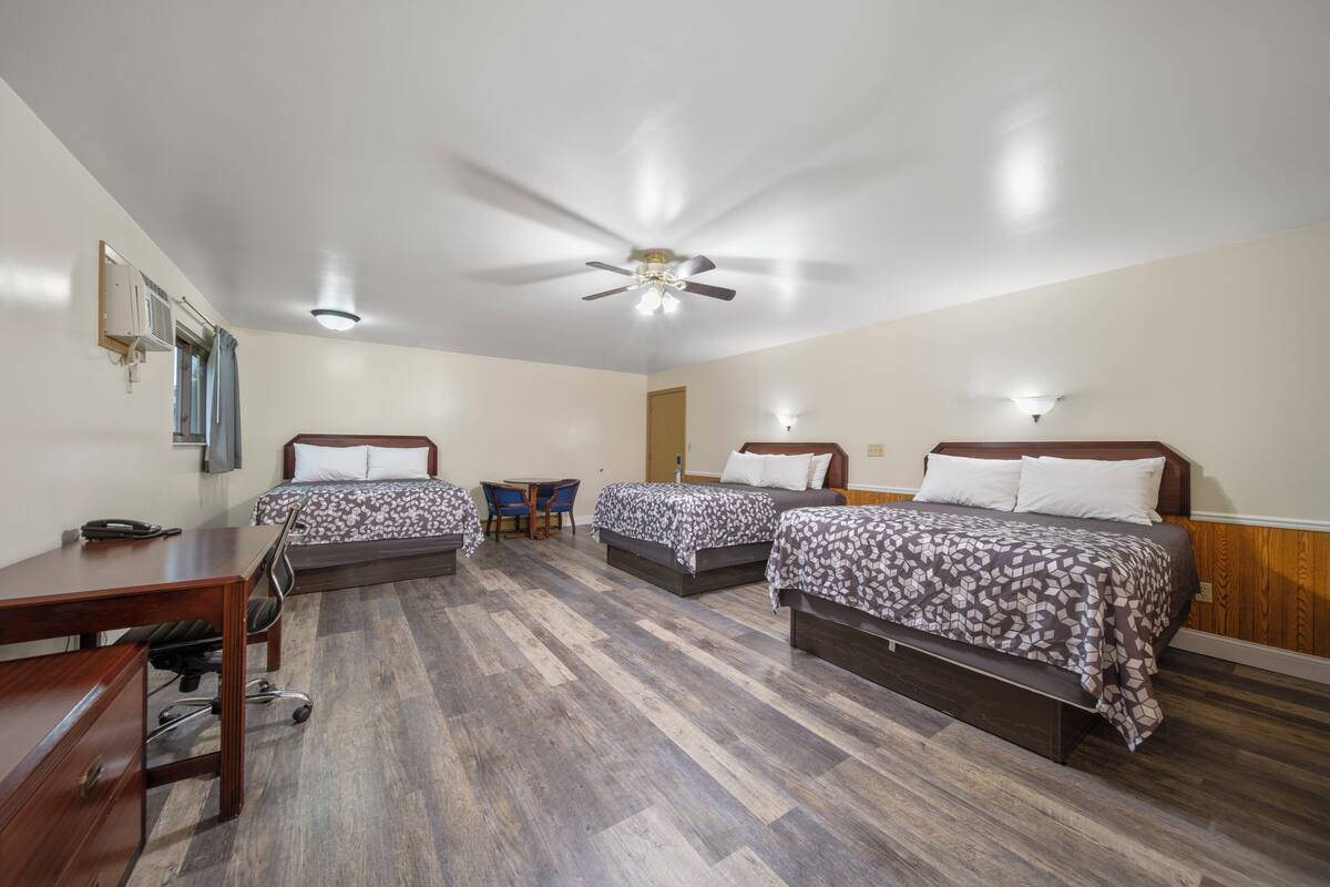 A hotel room with three beds, a desk, a chair, and a ceiling fan.
