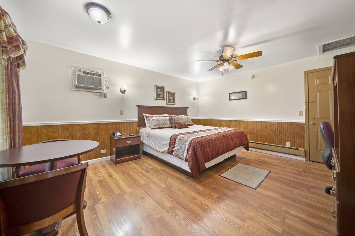 A bedroom with a bed, a desk, a chair, a ceiling fan, and a door.