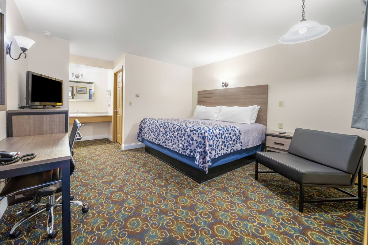 A hotel room with a bed, desk, chair, and a television.