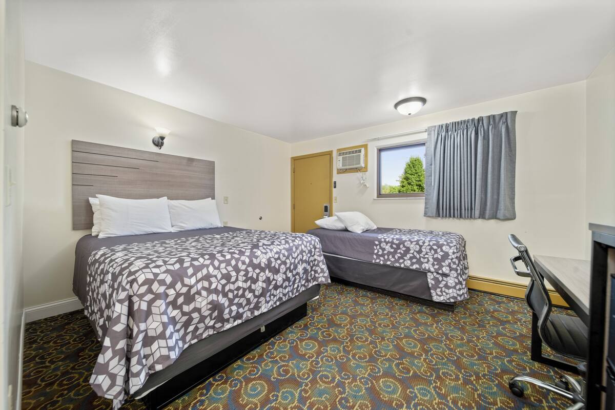 A hotel room with two beds, a desk, and a window with curtains.