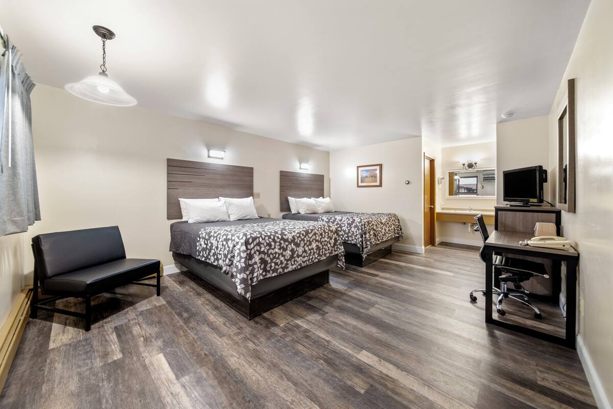 A hotel room with two beds, a desk with a chair, a television, and a small kitchenette.