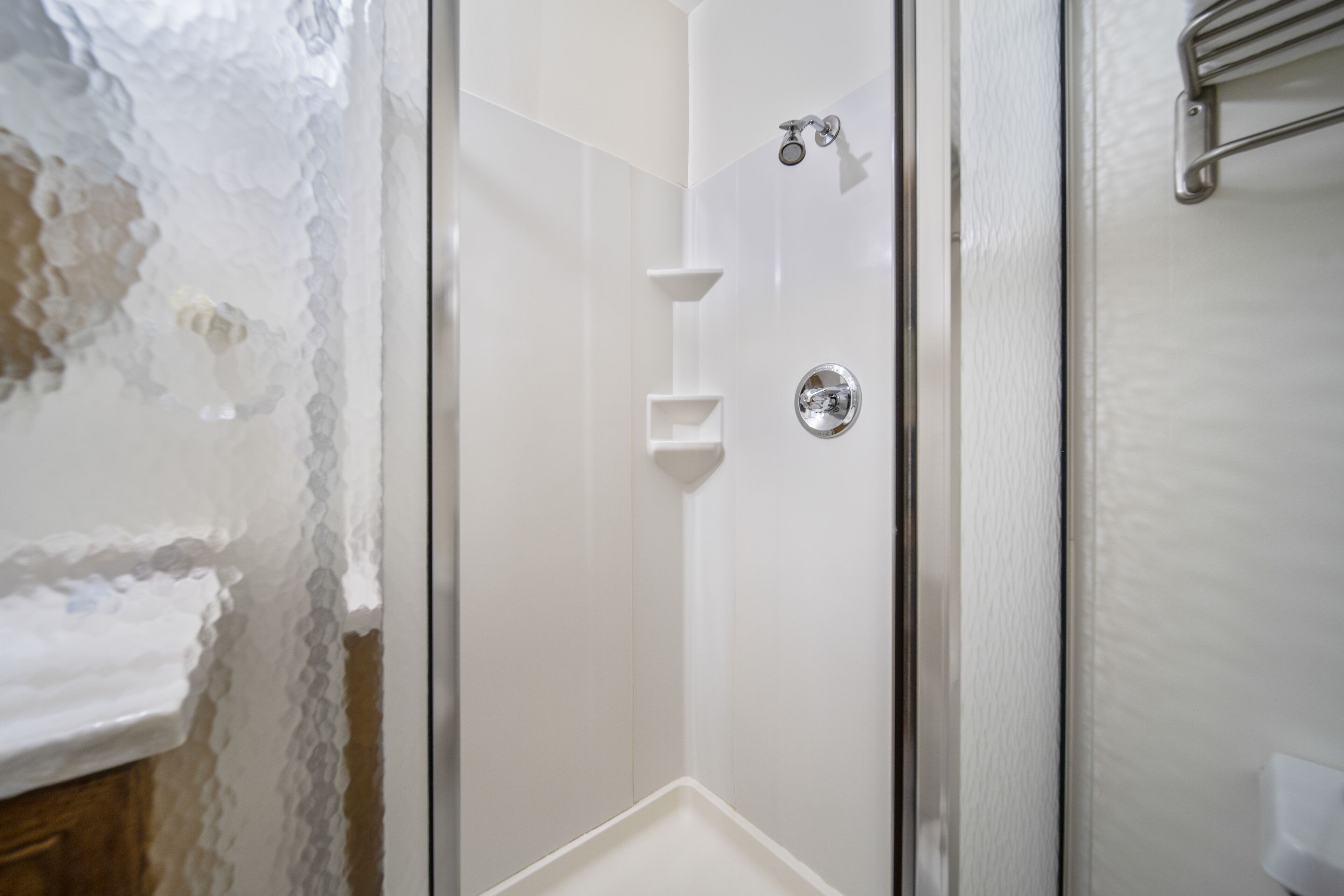 A modern bathroom with a glass shower enclosure, a white sink, and a towel rack.