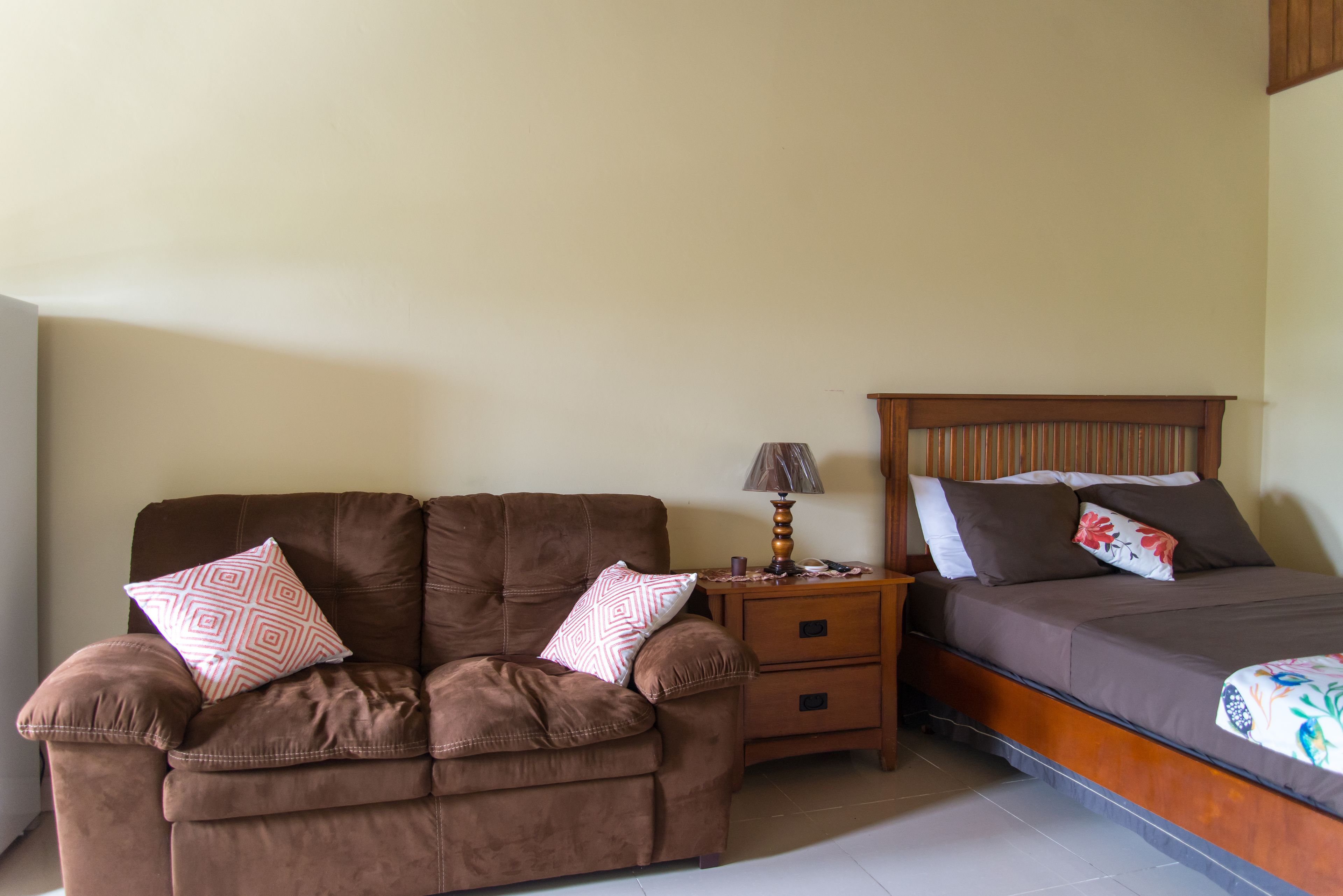 Une chambre à coucher avec un canapé marron, une table de chevet avec une lampe et un lit avec des oreillers.