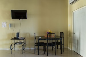 Una habitación con una televisión en la pared, un escritorio con ordenador y una mesa de comedor con sillas.