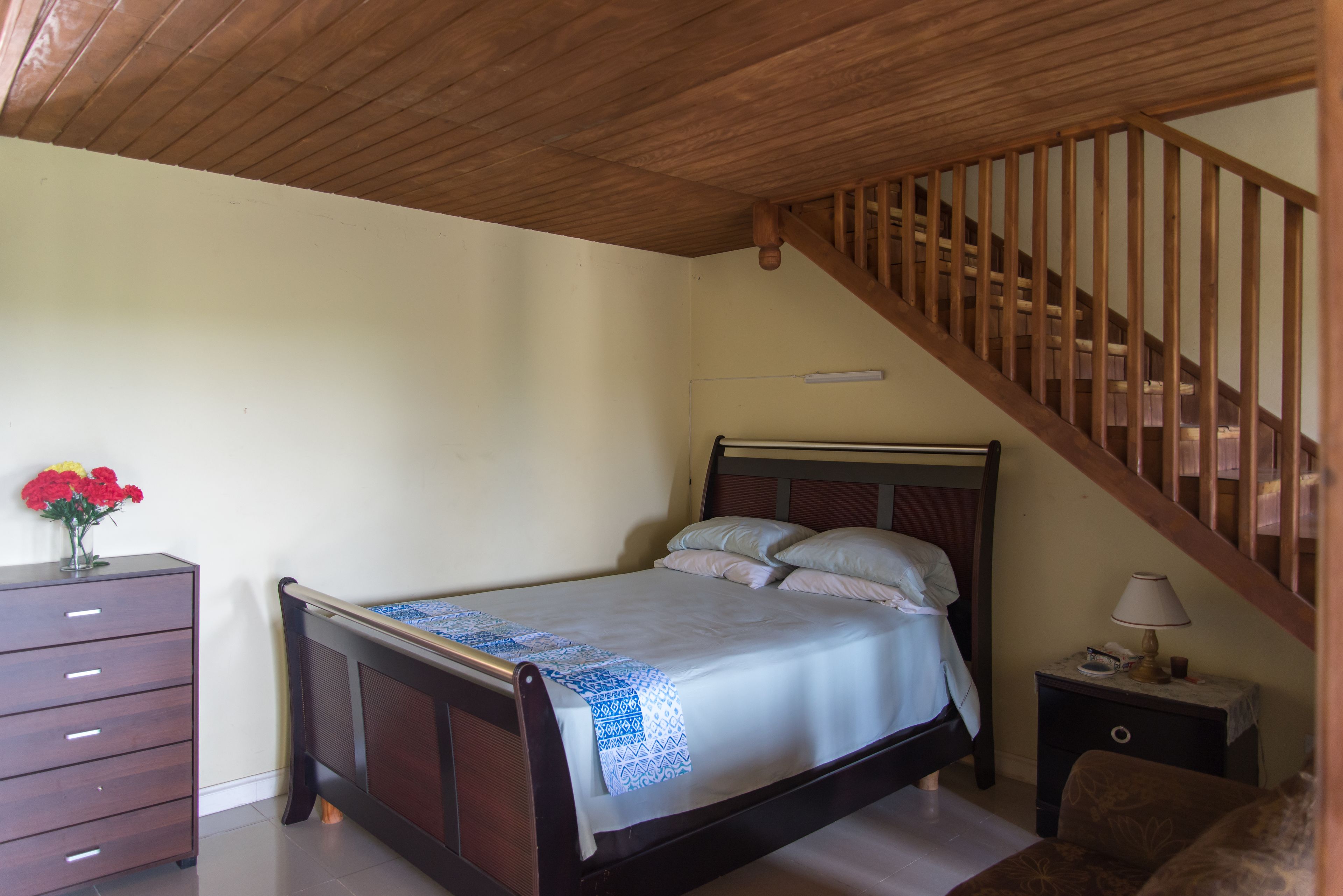 Un dormitorio con una cama de madera, una mesita de noche, un aparador y una escalera.