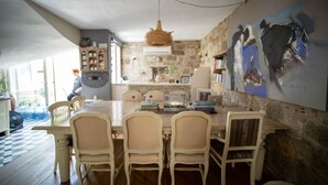 A dining area with a large table, four chairs, a hanging light fixture, and a stone wall with a painting. - Kallista Alaçatı (Cesme)