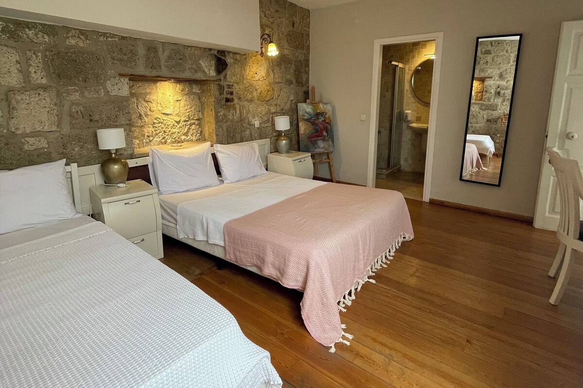 A bedroom with two beds, a stone wall, a wooden floor, and a mirror.