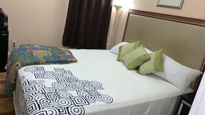A neatly made bed with a patterned bedspread and pillows, a bedside lamp, and a window with curtains.