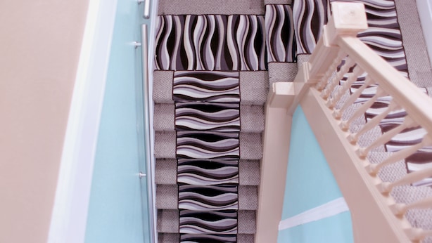 A close-up of a patterned wall with a textured design, a wooden railing, and a light-colored door frame.