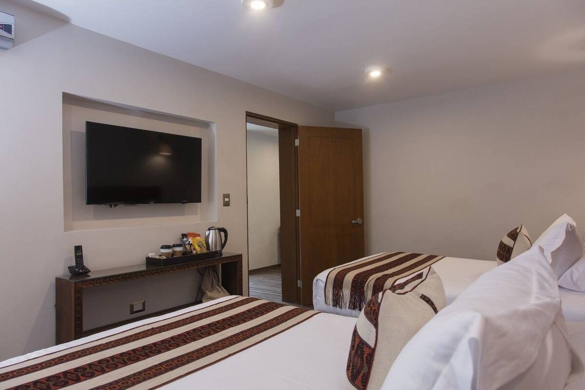 Een hotelkamer met twee bedden, een aan de muur bevestigde televisie, een koffiehoek en een houten deur.