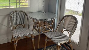 A corner room with a small round table and two wicker chairs, a window with blinds, and a door with a view of greenery outside. - Quiet Island Sanctuary, Private Studio, Sleep Deep, Walk to Beach (Vero Beach)