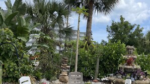 A garden with outdoor seating, including white and brown chairs, surrounded by various plants and a stone fountain. - Quiet Island Sanctuary, Private Studio, Sleep Deep, Walk to Beach (Vero Beach)