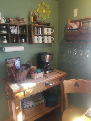 A kitchen with a coffee maker, mugs, and a basket on a wooden table.
