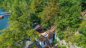 Ein abgelegenes Häuschen mit Holzterrasse und kleiner Veranda, umgeben von dichtem Wald und einem Gewässer.
