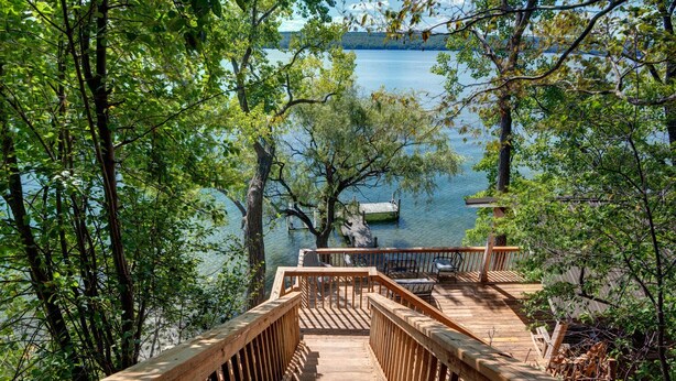 Eine Holzterrasse, die zu einem Steg über einem See führt, umgeben von Bäumen.
