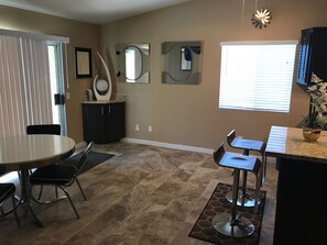 A dining area with a round table and chairs, a kitchen counter with a sink, and a window with blinds.