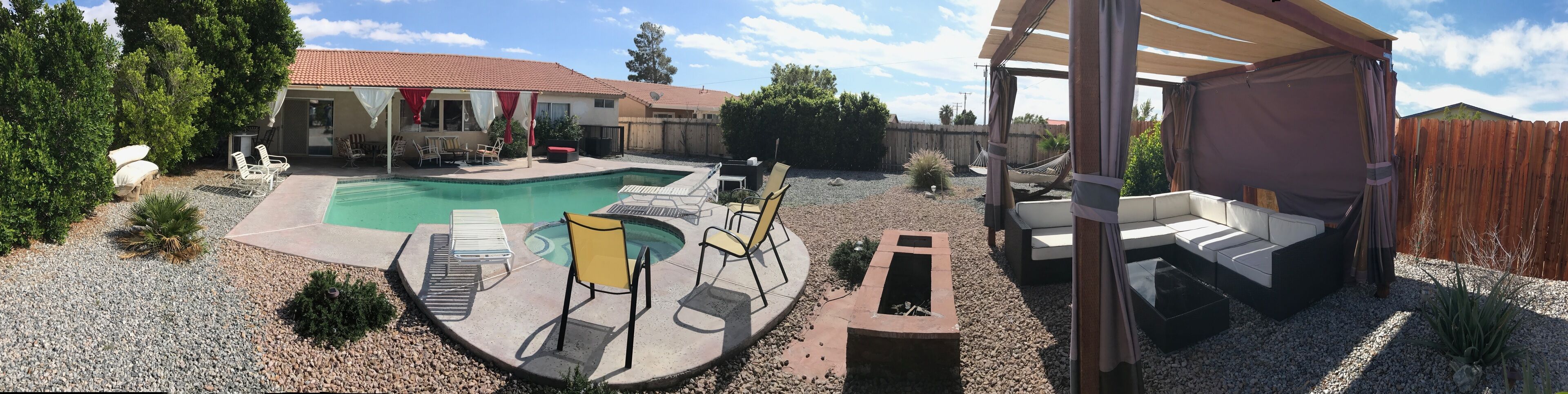Ein Garten mit Swimmingpool, Liegestühlen, einer überdachten Sitzgelegenheit und einem Holzzaun.