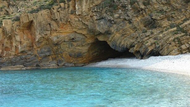 L'entrée d'une grotte côtière, avec une eau turquoise cristalline et une falaise rocheuse.