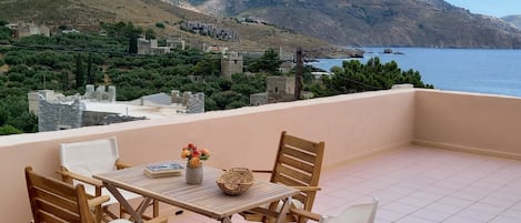 A terrace with a table and chairs overlooking a coastal landscape with hills and buildings.