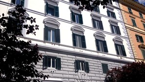 A multi-story building with a classical architectural style, featuring a central entrance with a wooden door and green shutters.