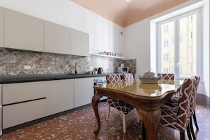A kitchen with a dining table and chairs, a microwave, and a window with a view of buildings.