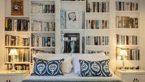 A neatly arranged bedroom with a large bed, two bedside lamps, and a bookshelf filled with books.