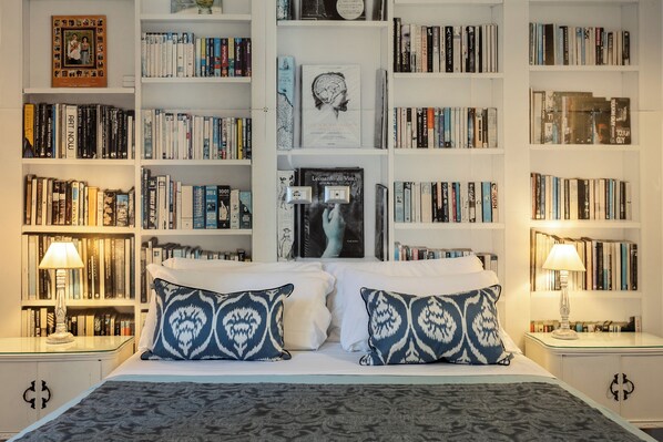 A neatly arranged bedroom with a large bed, two bedside lamps, and a bookshelf filled with books.