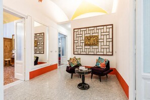 A hallway with a mirror, two armchairs, a small table, and a decorative wall panel.