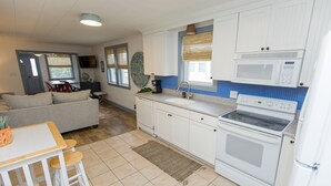Een compacte keuken met witte kastjes, een magnetron en een fornuis. Er is een eethoek met een tafel en stoelen.