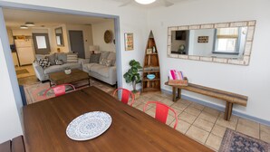 Een eethoek met een houten tafel, rode stoelen en een wit bord. Er is een plafondventilator, een houten bank en een spiegel aan de muur.