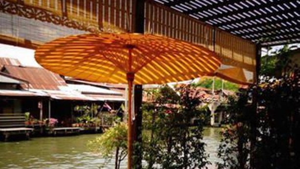 Un área de estar al aire libre con mesa y silla de madera, un paraguas grande y vistas a un cuerpo de agua y vegetación.