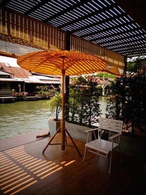 Un área de estar al aire libre con mesa y silla de madera, un paraguas grande y vistas a un cuerpo de agua y vegetación.