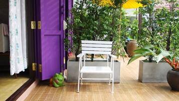 Une pièce avec une porte violette, une chaise blanche, un coussin bleu et des plantes en pot.