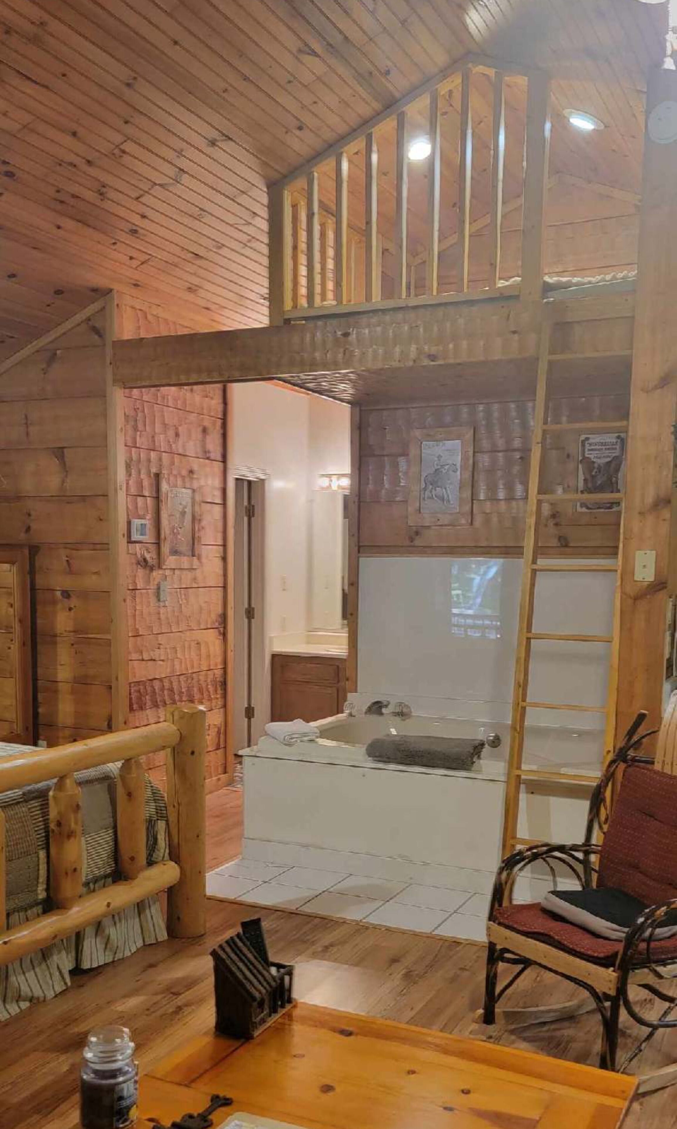 Interior d'una cabana amb sostre de fusta, zona d'altell amb escala, banyera i un banc de fusta.