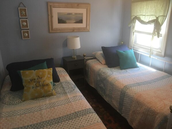 A bedroom with two beds, a nightstand, a lamp, a framed picture on the wall, and a window with curtains.
